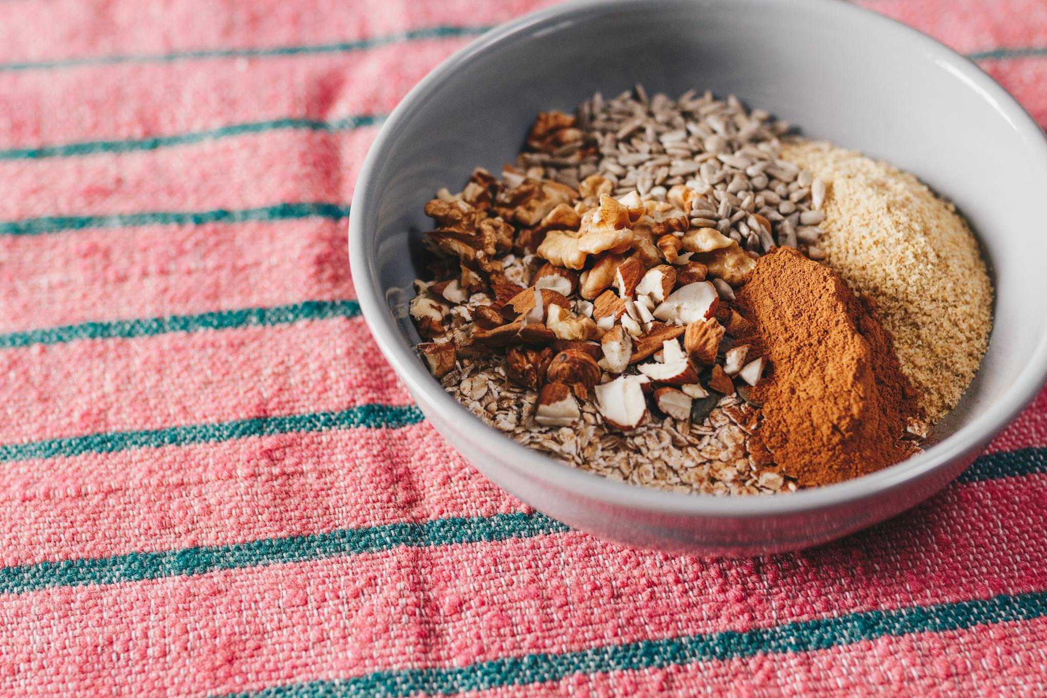 A mix of seeds, nuts, and spices in a bowl on a pink textured cloth, showcasing healthy food.