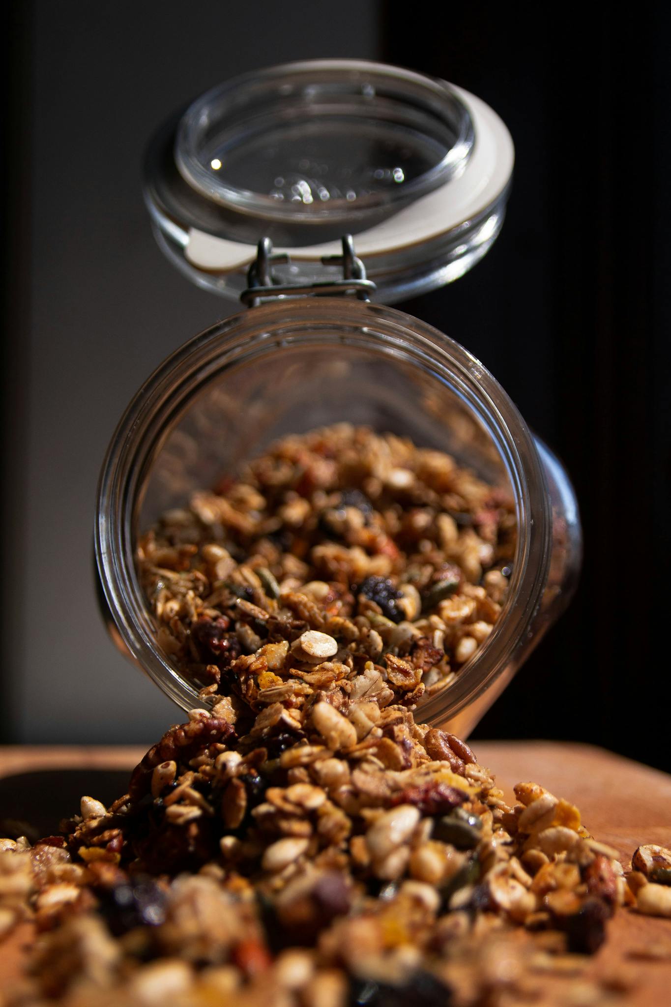 Close-up of a glass jar spilling healthy granola mix with nuts and seeds on a wooden surface.