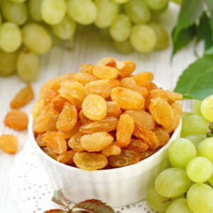 Dried raisins in a white bowl and fersh grape on the wooden background