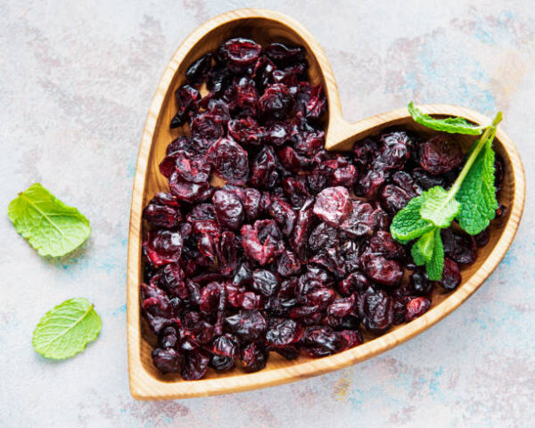 Wooden bowl full of sweet dried cherries on grey concrete background