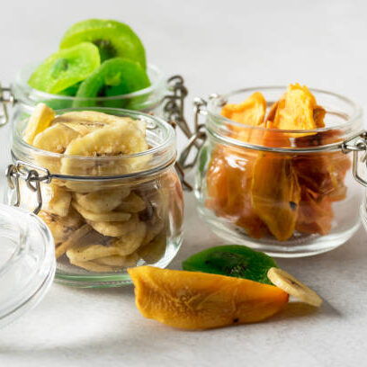 Green kiwi banana persimmon fruit preserved in glass jars on gray background